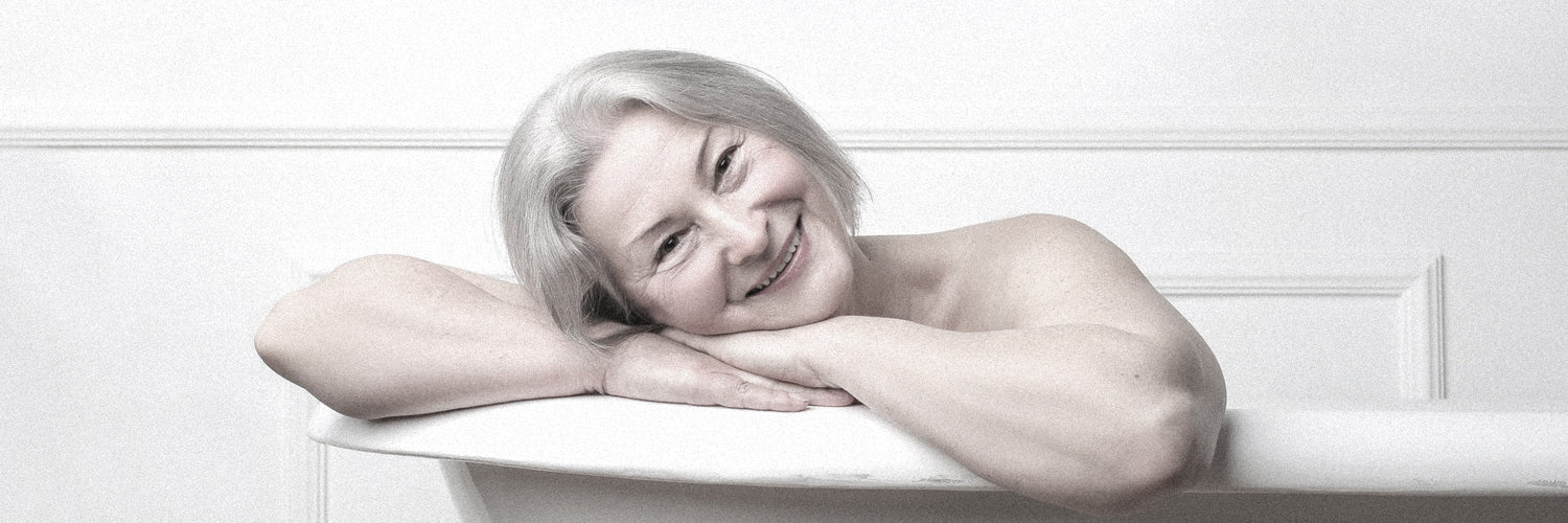 a senior woman rests on the edge of a bathtub